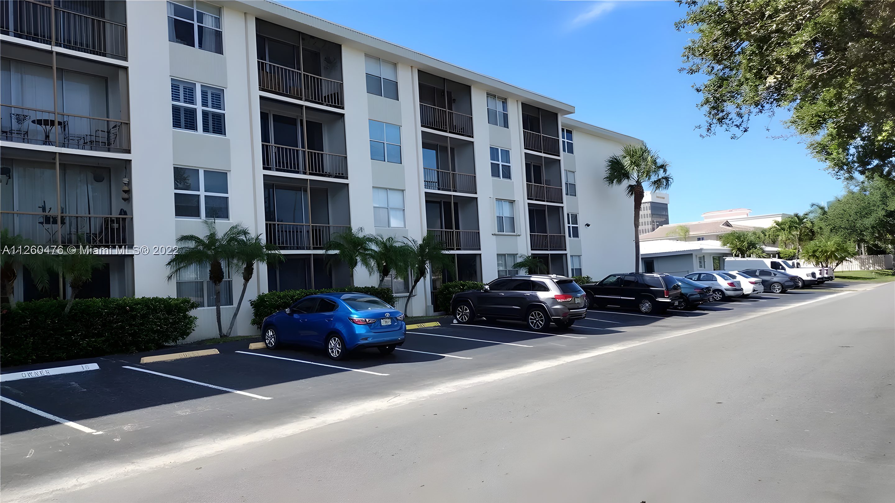 Coral Ridge East from 21st Avenue: four floors of white stucco behind palms and the association's parking.